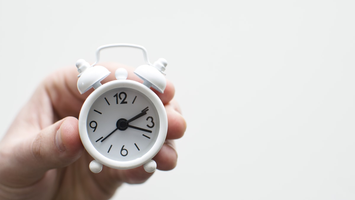 A hand switching off an analogue alarm clock on a bedside table