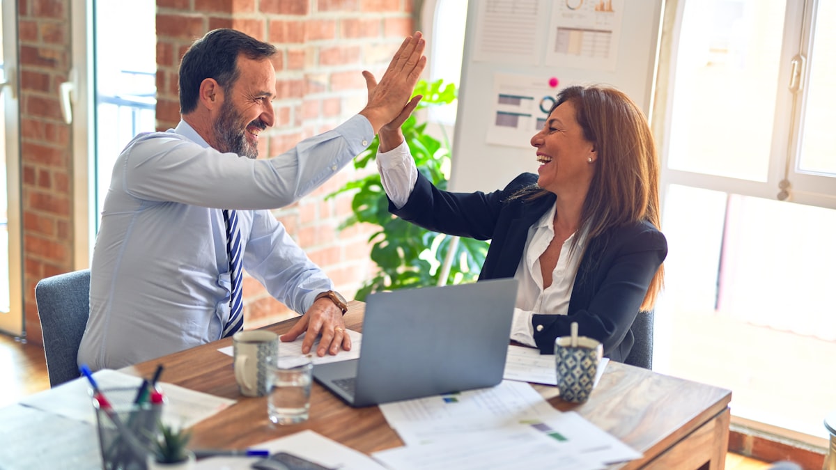 Two colleagues high-fiving, satisfied, in front of their work plan