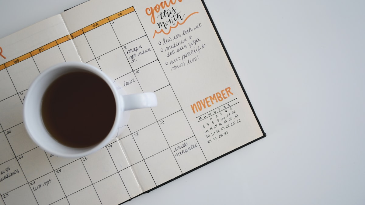 Coffee cup resting on a planner open to the monthly calendar