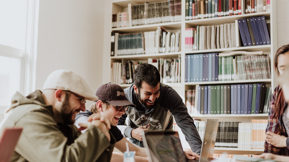 Group of students laughing around a laptop in a library