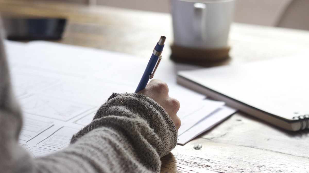 Hand taking short notes in a notebook next to a coffee cup